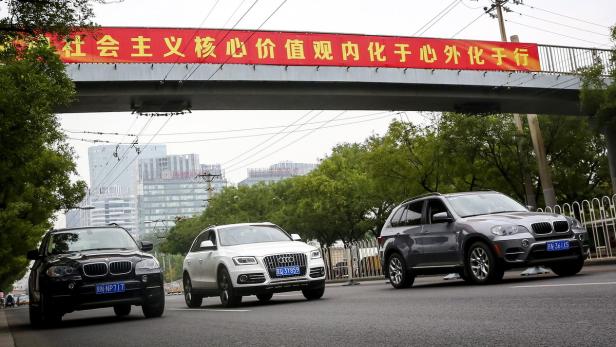 Drei Autos fahren unter einer Brücke mit einem chinesischen Banner hindurch.