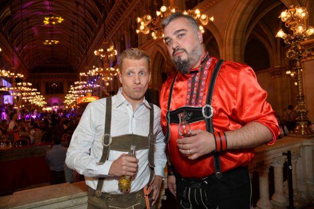 Zwei Männer in Tracht mit Bierflaschen in einem festlichen Saal.