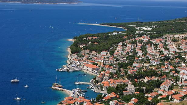 Blick auf eine Küstenstadt mit roten Dächern und blauem Meer.