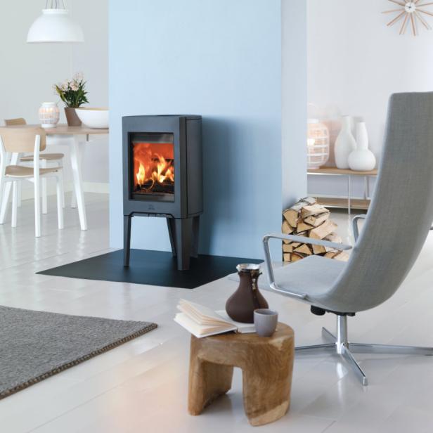 Ein Kaminofen steht in einem hellen Wohnzimmer mit Holzboden.