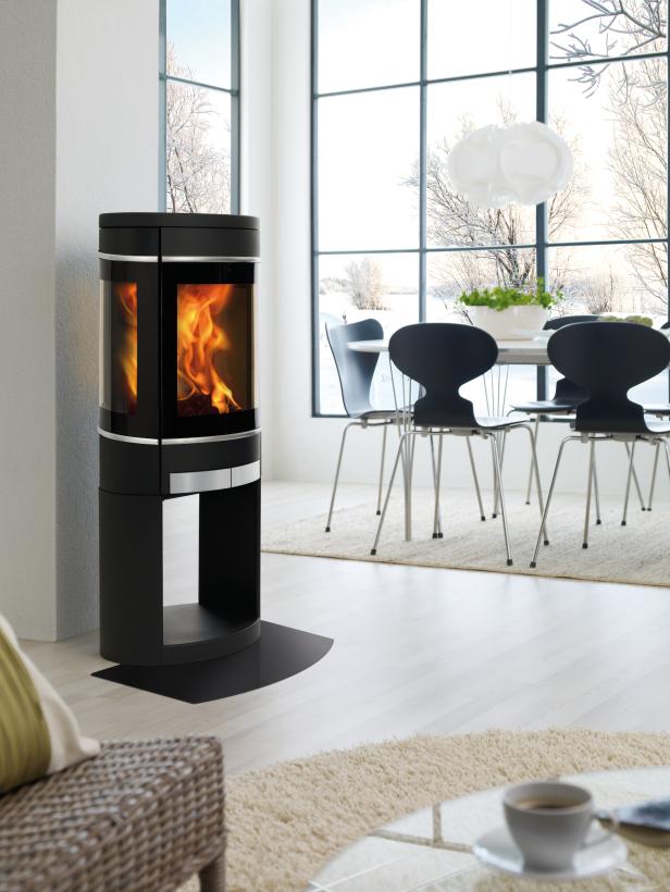 Ein moderner Kaminofen steht in einem hellen Wohnzimmer mit Blick auf eine Winterlandschaft.
