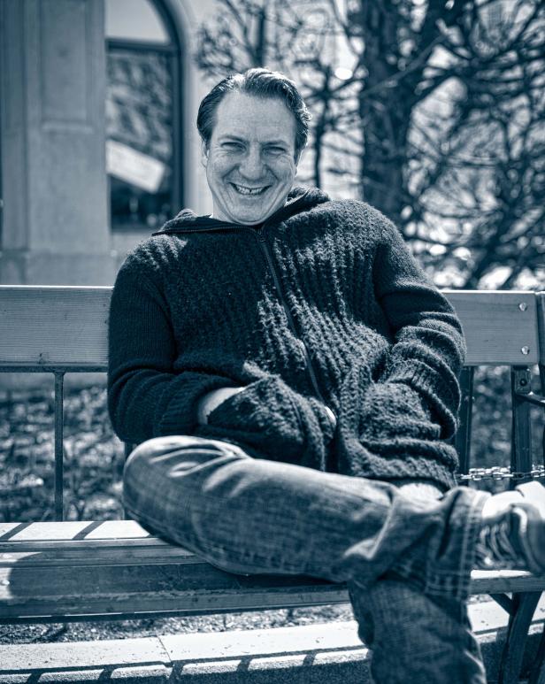 Ein lächelnder Mann sitzt auf einer Parkbank.