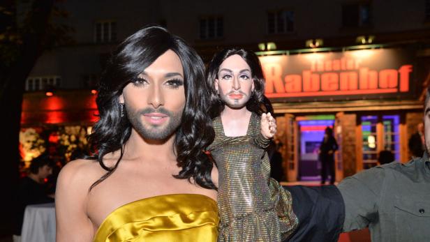Conchita Wurst hält eine Puppe von sich selbst vor dem Theater Rabenhof.