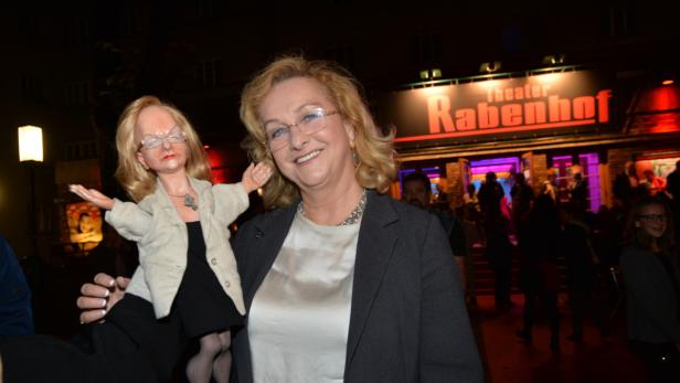 Eine Frau hält eine Puppe, die ihr ähnelt, vor dem Theater Rabenhof.