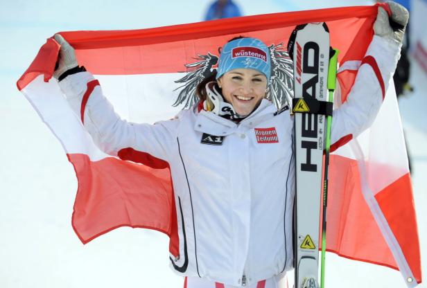 Eine Skirennläuferin hält eine österreichische Flagge und ihre Skier in die Höhe.