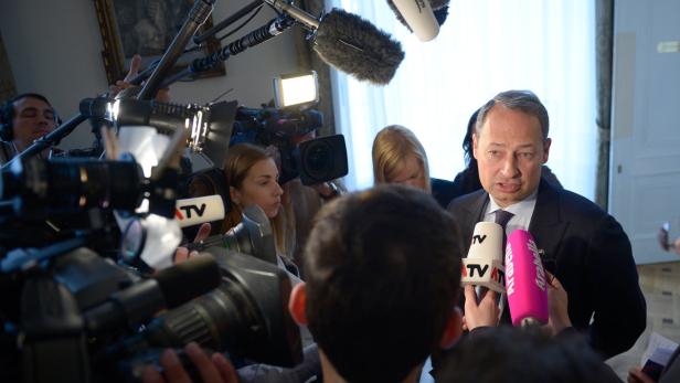 Ein Mann im Anzug spricht in eine Vielzahl von Mikrofonen vor einer Gruppe von Reportern.