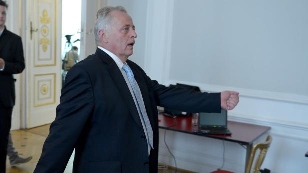 Ein Mann im Anzug gestikuliert in einem formellen Raum.