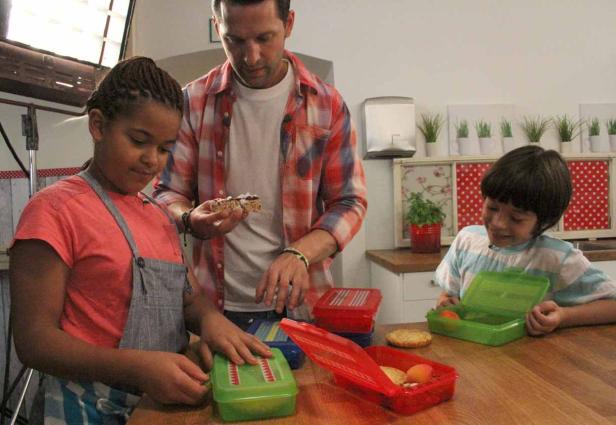 Ein Mann und zwei Kinder bereiten eine Lunchbox in einer Küche vor.