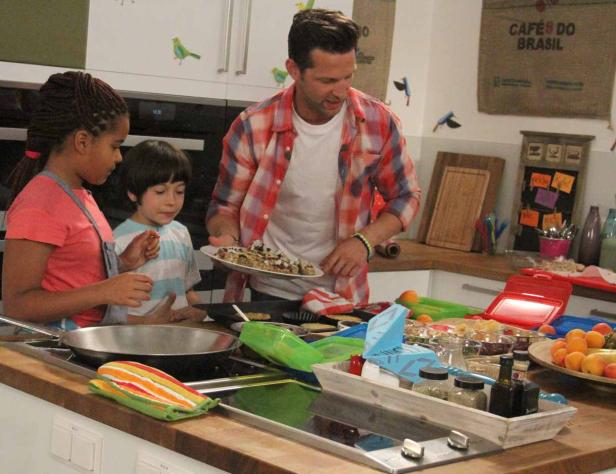 Ein Mann kocht mit zwei Kindern in einer Küche.