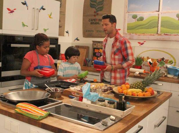 Zwei Kinder und ein Mann bereiten in einer Küche eine Mahlzeit zu.