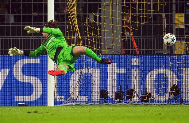 Ein Torwart in grüner Sportkleidung springt, um einen Fußball zu halten.