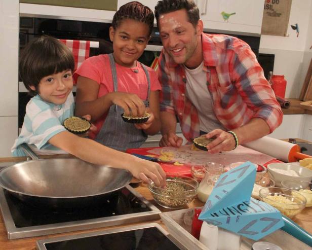 Ein Mann und zwei Kinder bereiten in einer Küche kleine Quiches zu.
