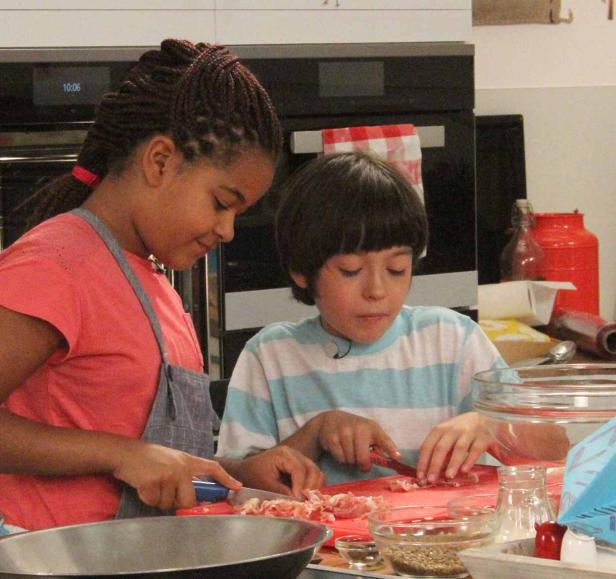 Zwei Kinder stehen in einer Küche und schneiden Zutaten.