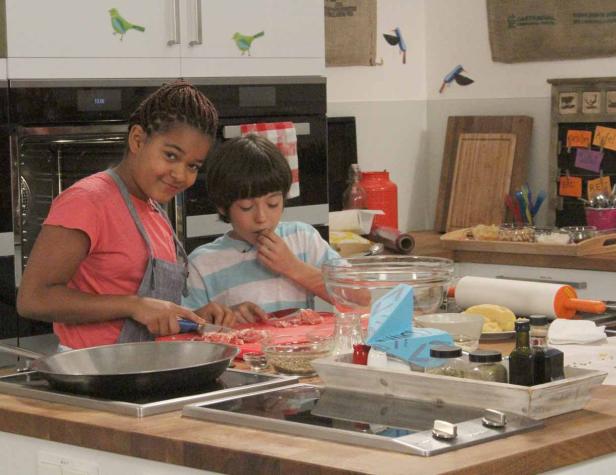 Zwei Kinder bereiten gemeinsam Essen in einer Küche zu.