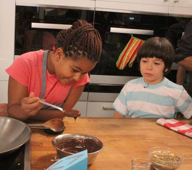 Zwei Kinder betrachten schmelzende Schokolade in einer Küche.