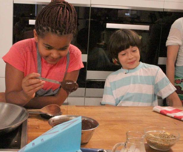 Zwei Kinder stehen in einer Küche und bereiten Schokoladendessert zu.