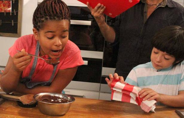 Ein Mädchen probiert Schokoladensoße, während ein Junge ein Küchentuch hält.