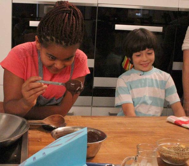 Zwei Kinder stehen in einer Küche und bereiten Schokoladenleckereien zu.