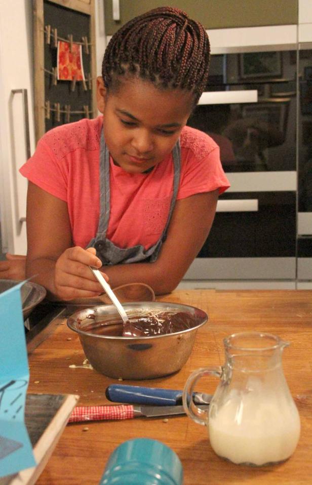 Ein Mädchen rührt Schokolade in einer Schüssel mit einem Löffel.