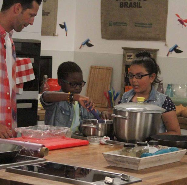 Zwei Kinder kochen mit Hilfe eines Mannes in einer Küche.