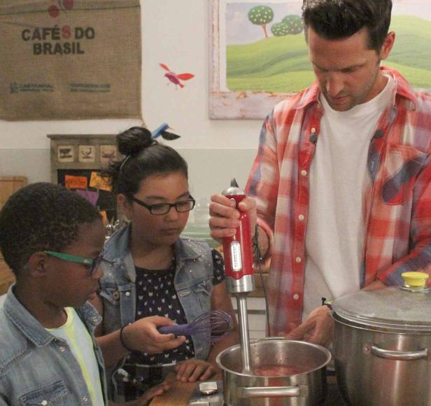 Ein Mann mixt mit Kindern eine rote Flüssigkeit in einem Topf.