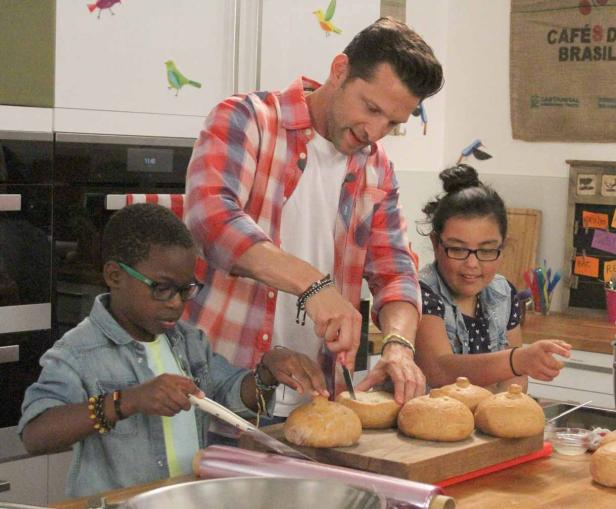 Ein Mann und zwei Kinder stehen in einer Küche und bereiten gefüllte Brötchen zu.