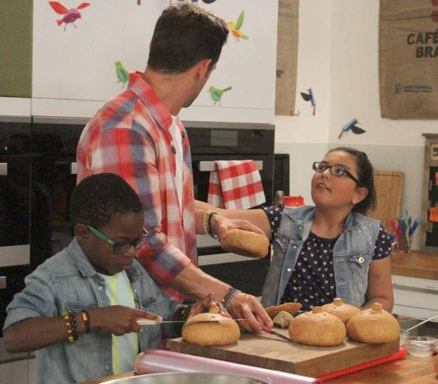 Ein Mann mit zwei Kindern bereitet in einer Küche gefüllte Brötchen zu.