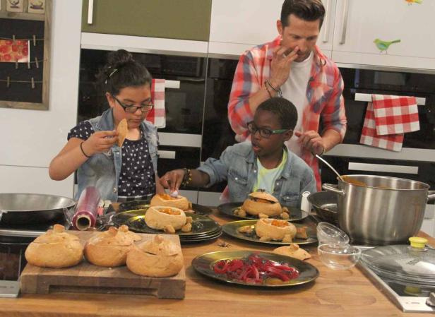 Zwei Kinder und ein Mann bereiten Kürbissuppe in Brottöpfen zu.