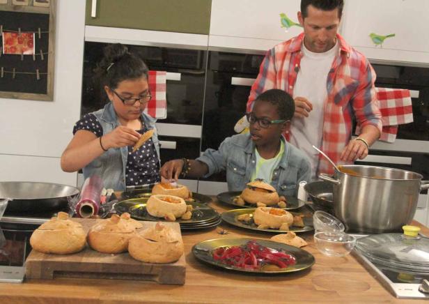 Zwei Kinder und ein Mann bereiten Kürbissuppe in Brottöpfen zu.