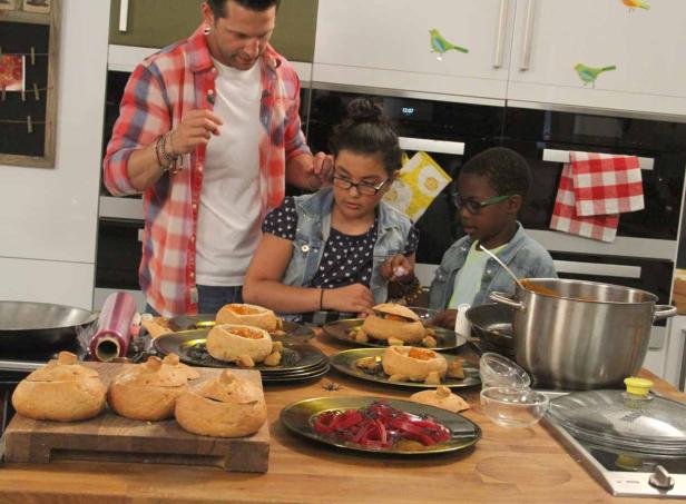Ein Mann und zwei Kinder bereiten Kürbissuppe in Brottöpfen zu.