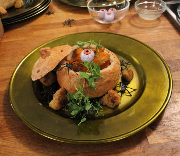 Eine Kürbissuppe wird in einem Brotlaib mit einem Augapfel serviert, dekoriert mit Spinnen und Erbsensprossen.