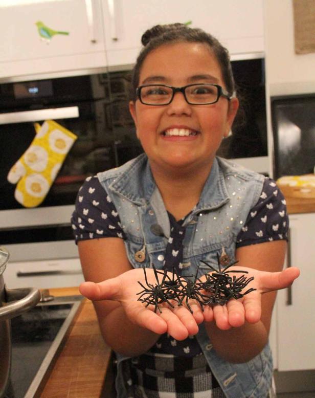 Ein Mädchen hält eine Handvoll schwarzer Plastikspinnen in ihren Händen.