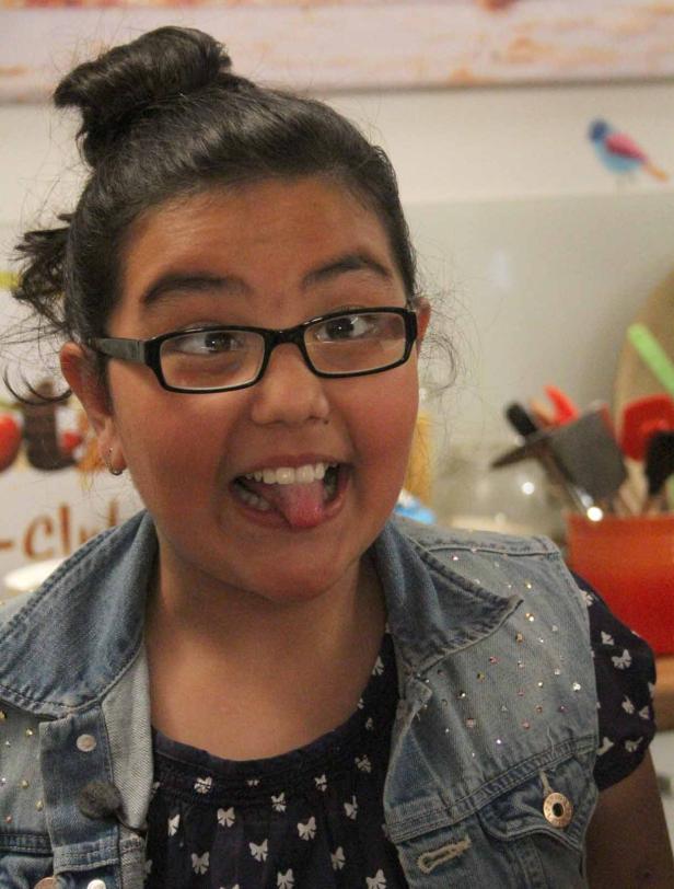 Ein junges Mädchen mit Brille streckt die Zunge heraus.