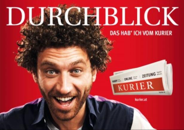 Ein Mann lächelt neben einer Ausgabe der Zeitung „Kurier“ vor rotem Hintergrund.