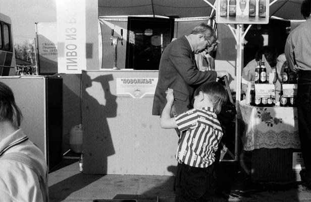 Ein Mann und ein Kind stehen an einem Bierstand mit der Aufschrift „ПОВОЛЖЬЕ“.
