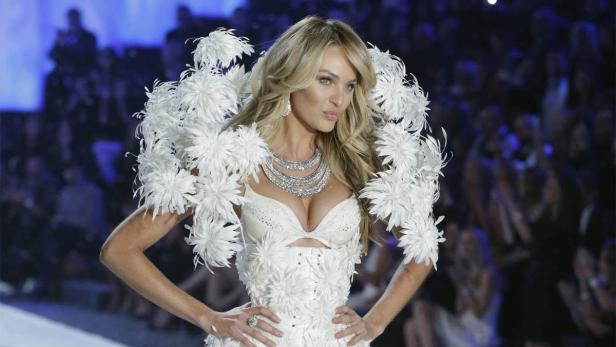 Ein Model mit blonden Haaren trägt ein weißes Federkostüm und eine Halskette auf dem Laufsteg.