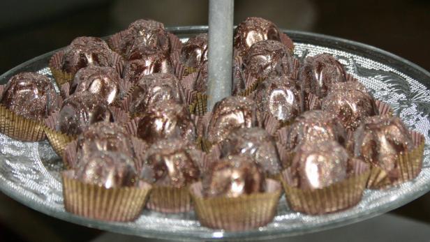 Eine Auswahl glitzernder Pralinen in goldenen Papierförmchen auf einer Etagere.