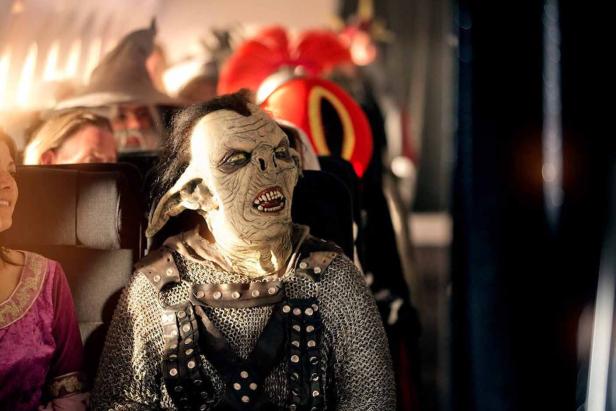 Ein Mann in einem Ork-Kostüm sitzt in einem Bus oder Zug.