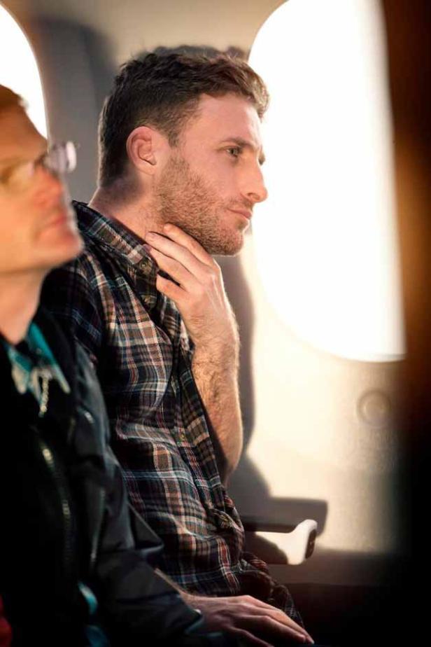 Ein Mann im Flugzeug blickt aus dem Fenster und hält sich an den Hals.