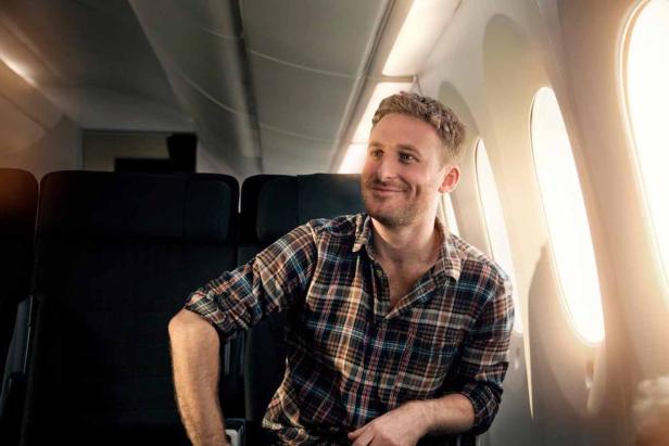 Ein lächelnder Mann sitzt in einem Flugzeug am Fenster.