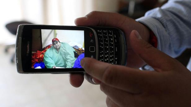 Eine Person betrachtet ein Foto einer anderen Person auf einem älteren Blackberry-Smartphone.