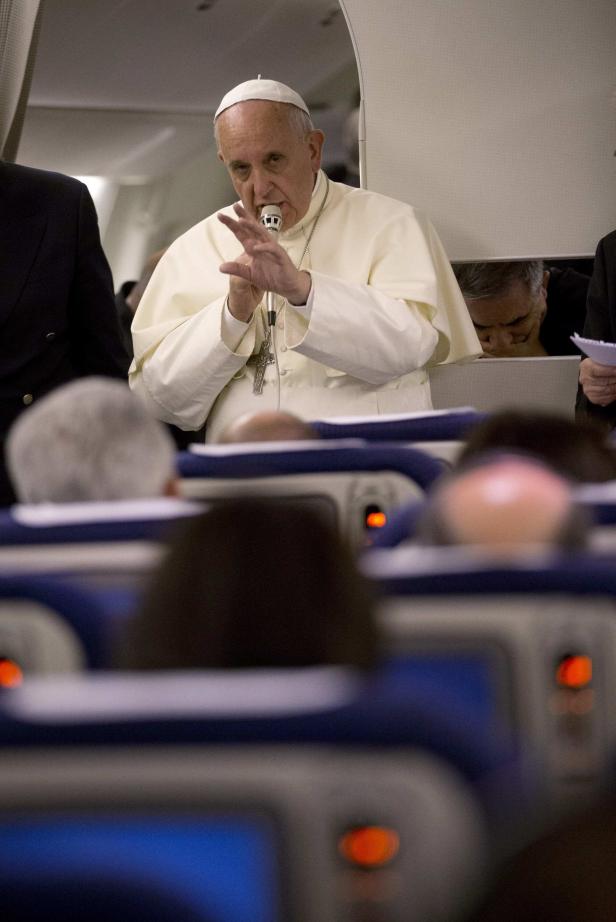 Papst Franziskus spricht in einem Flugzeug in ein Mikrofon.