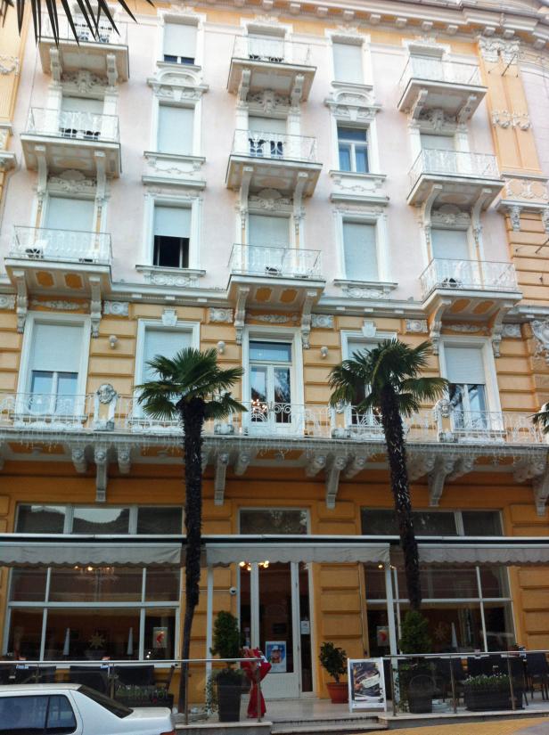 Ein gelbes Gebäude mit weißen Balkonen und zwei Palmen im Vordergrund.