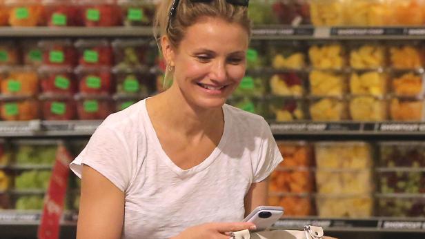 Cameron Diaz lächelt in einem Supermarkt und schaut auf ihr Handy.