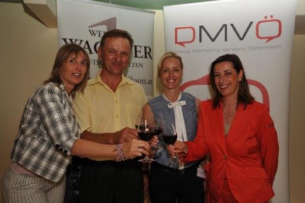 Vier Personen stoßen mit Rotwein vor Bannern von „Wein Wagner“ und DMVÖ an.