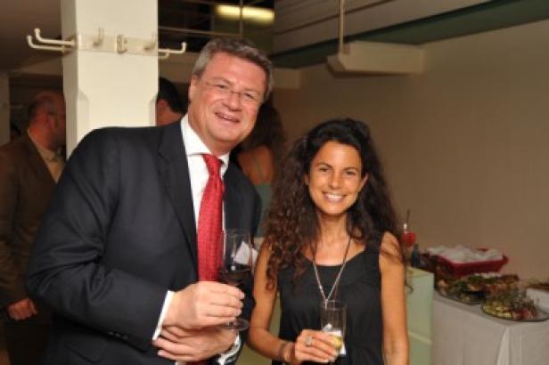 Ein Mann im Anzug und eine Frau lächeln mit Getränken in der Hand.