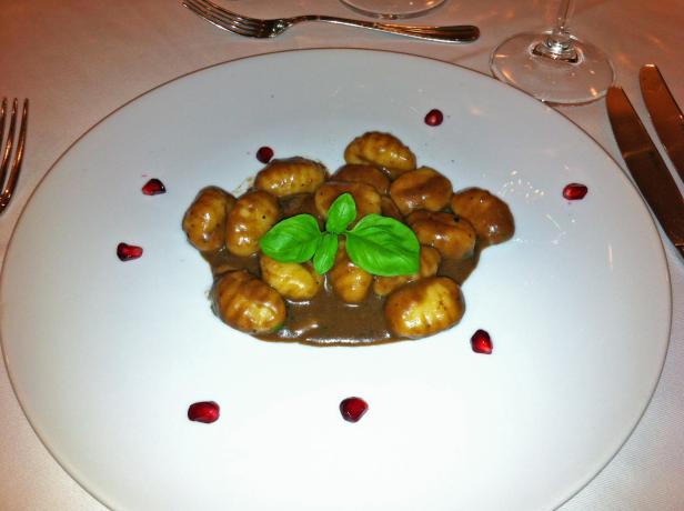 Gnocchi mit brauner Soße und Basilikum auf einem Teller, garniert mit Granatapfelkernen.