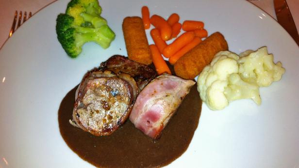 Ein Teller mit Fleisch, Kroketten, Karotten, Brokkoli und Blumenkohl in dunkler Soße.