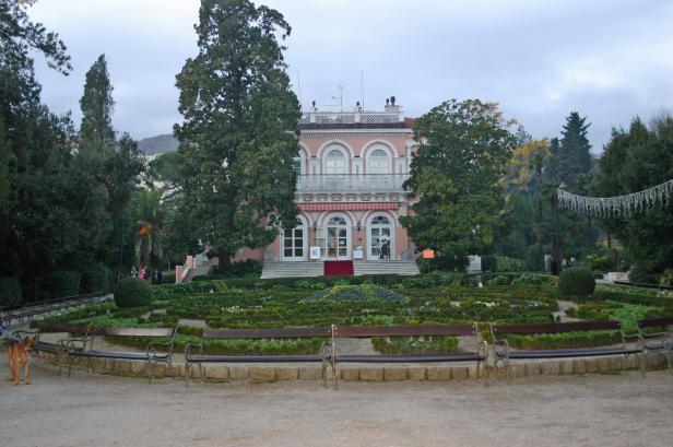 Ein rosafarbenes Gebäude mit einem gepflegten Garten im Vordergrund.