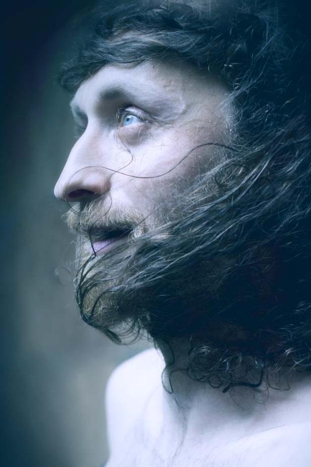 Ein Mann mit Bart und langen, dunklen Haaren blickt zur Seite.